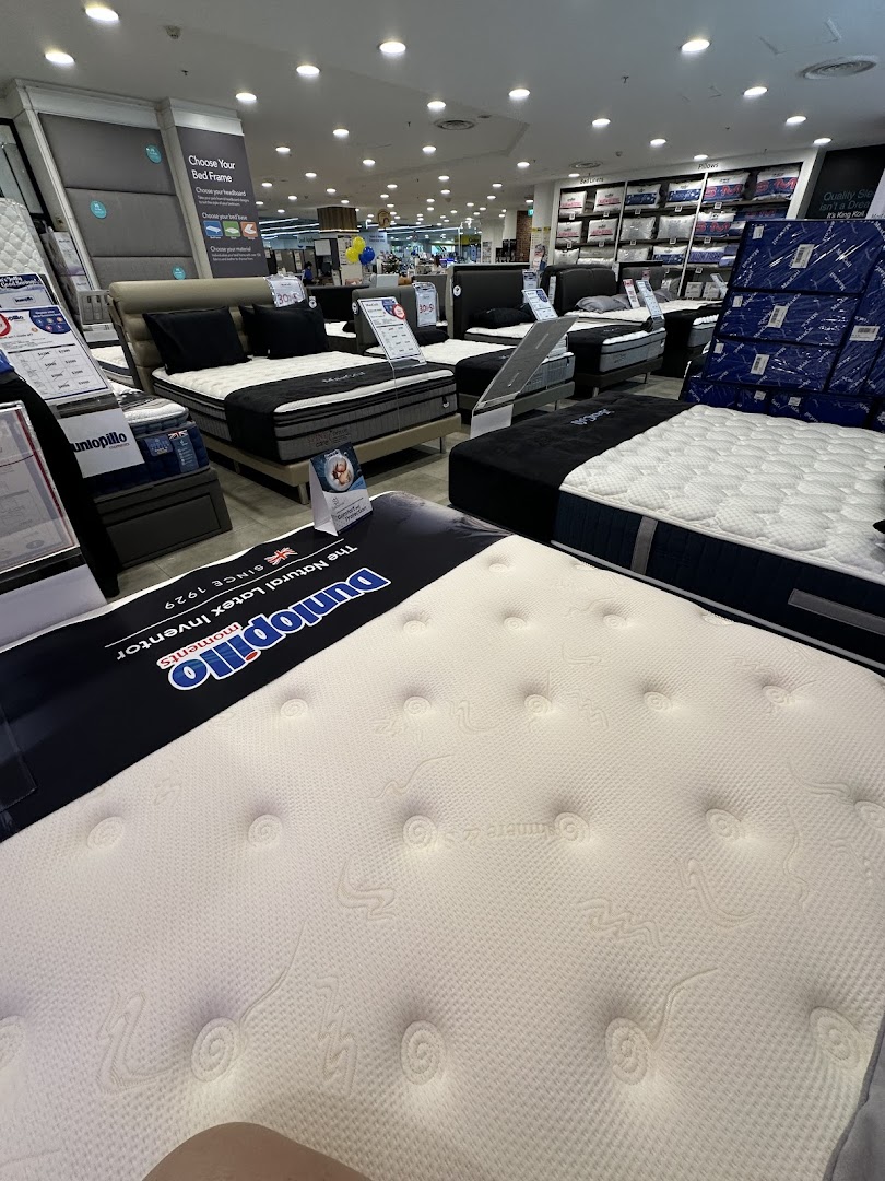 An interior view of COURTS, showcasing a wide selection of mattresses and bed frames in the bedding department.