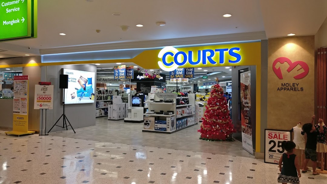 The brightly lit entrance of COURTS electronics store, featuring a festive Christmas tree and sale promotions.
