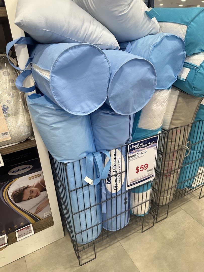 A retail display of pillows and bolsters, including light blue packaged items, in wire bins at COURTS.
