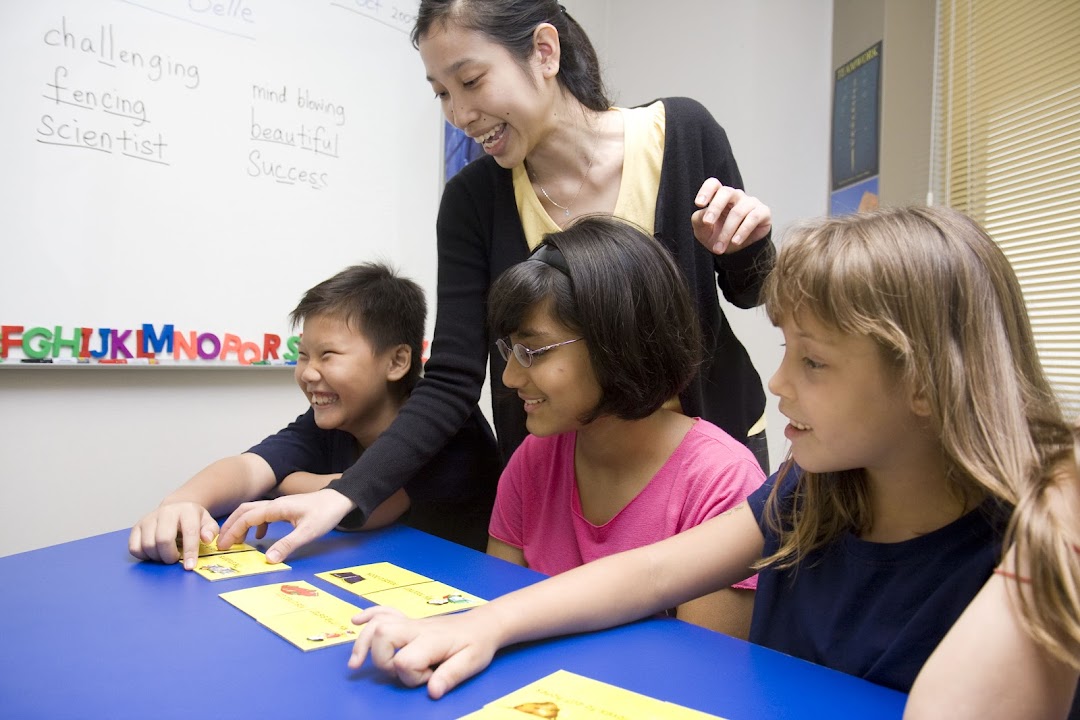A teacher guides three smiling students engaged in a learning activity at DAS International.