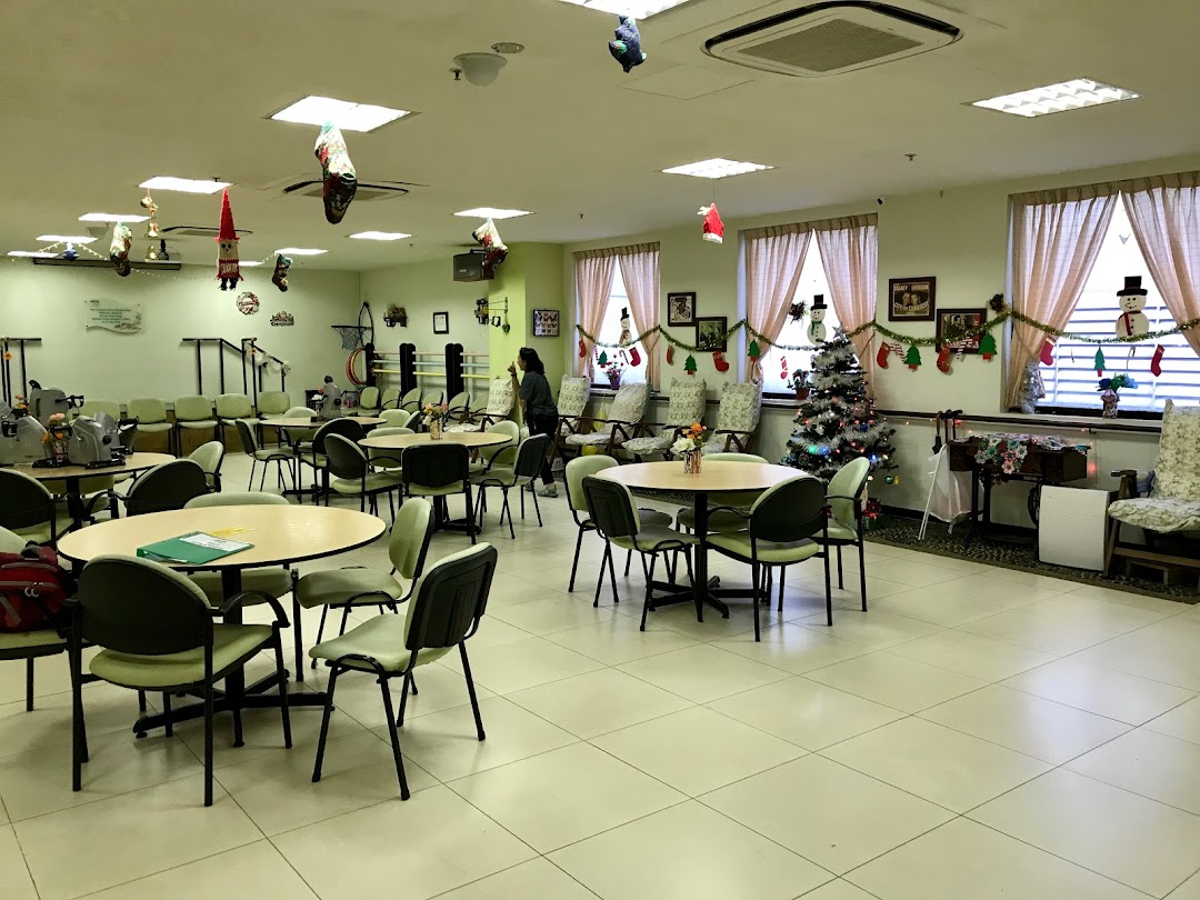 A spacious, festive common area at Dementia Singapore's New Horizon Centre, featuring tables, chairs, and exercise equipment.