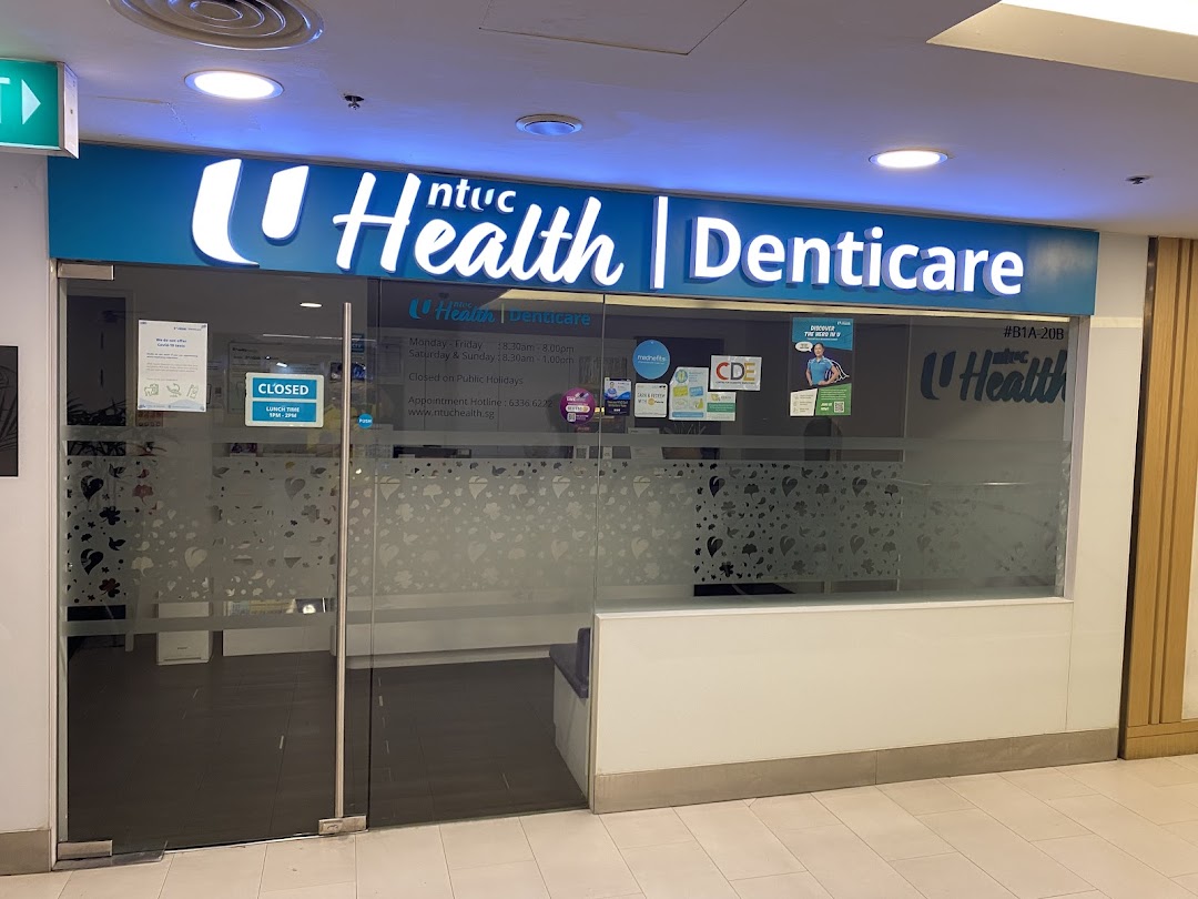 The storefront of NTUC Health Denticare, a dental clinic, featuring its illuminated sign and glass entrance.