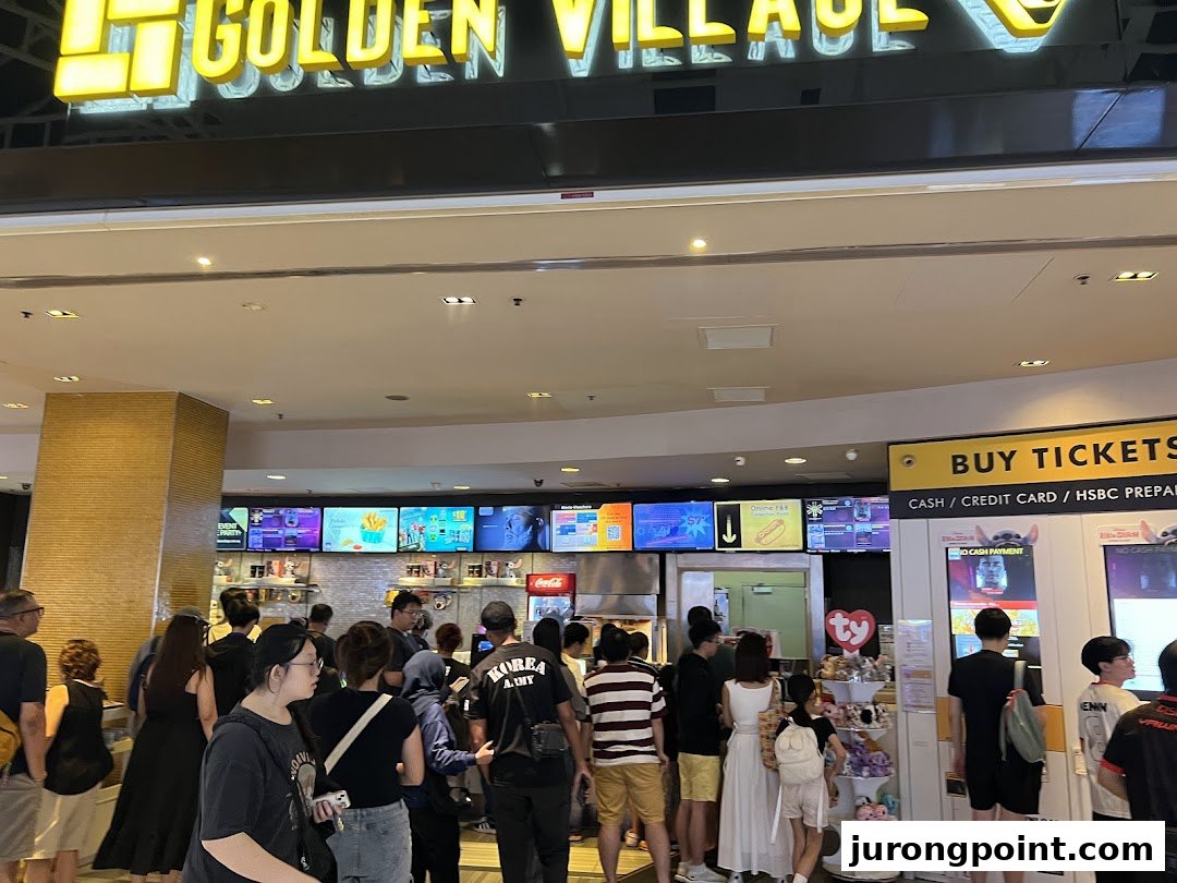 A bustling mall entrance area featuring a cinema facade, ticket kiosks, and people queuing.