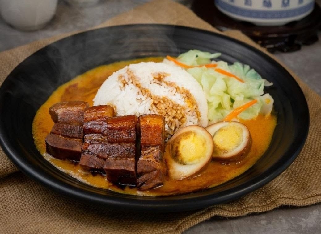 A delicious plate of braised pork belly with rice, eggs, and vegetables in a rich sauce.