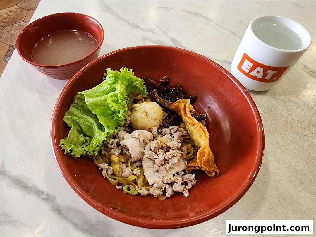 A vibrant bowl of noodles with minced meat, vegetables, and a fried wonton, served with soup and water.