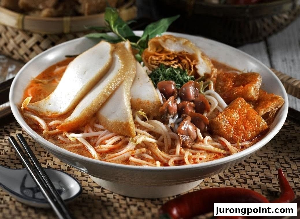 A vibrant bowl of spicy laksa noodles with fish cakes, cockles, and tofu puffs.