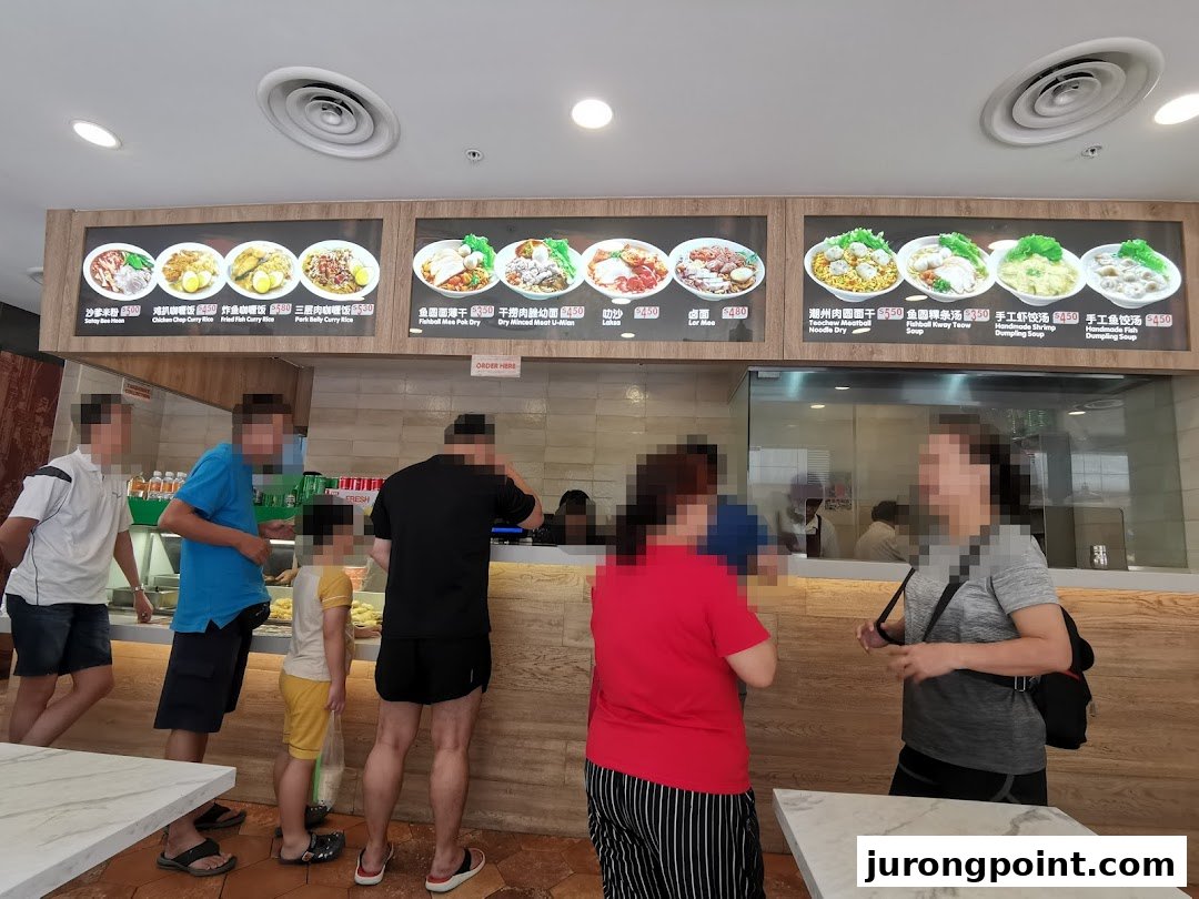 Customers queue at a bustling food stall with digital menu boards displaying various Asian dishes.