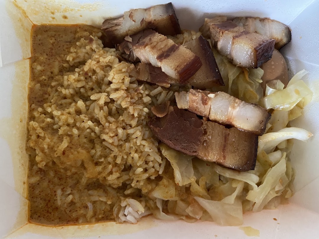 A close-up of a takeaway meal featuring rice with curry, braised pork belly, and cabbage.
