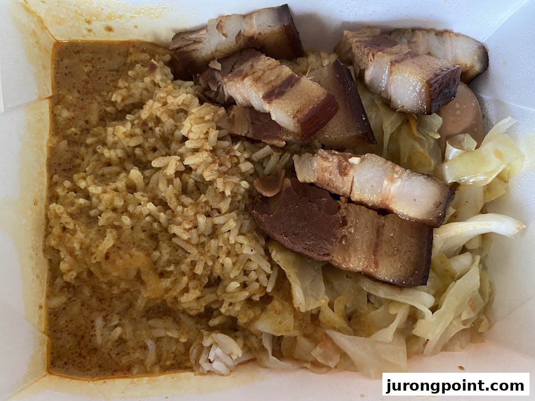 A close-up of a takeaway meal featuring rice with curry, braised pork belly, and cabbage.