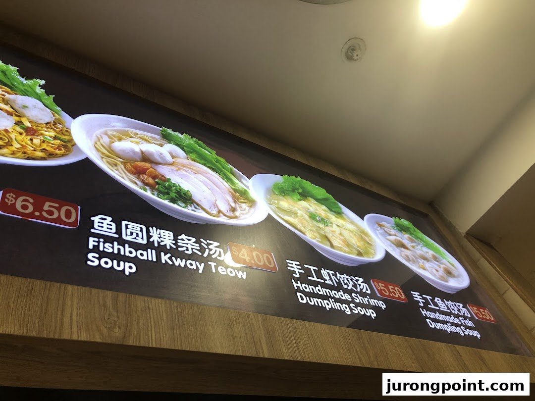A brightly lit menu board displaying various noodle and dumpling soup dishes with their prices.