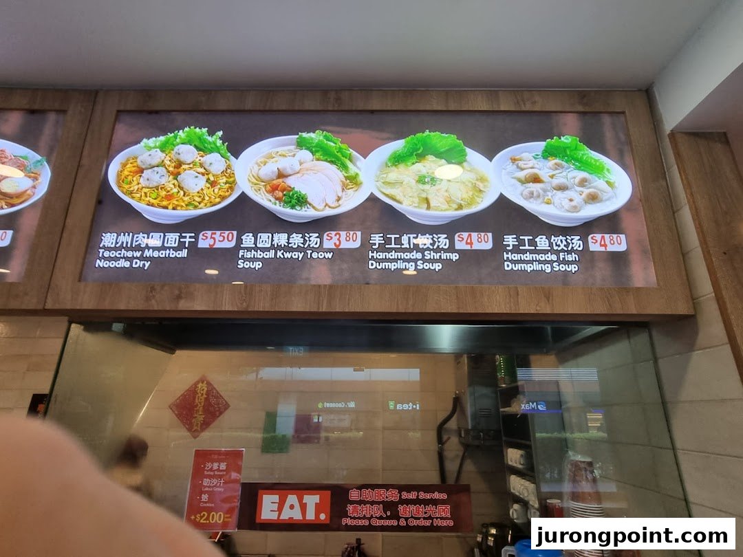 A brightly lit menu board displaying various noodle and dumpling dishes with prices at 'EAT.'