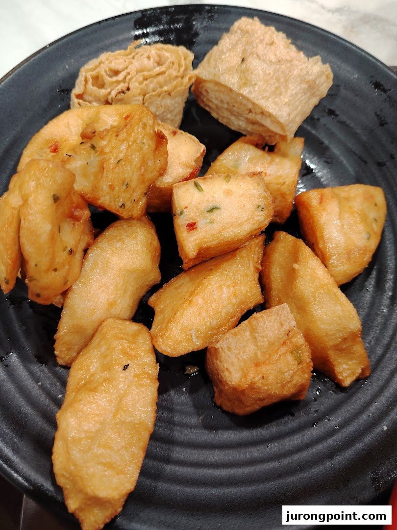 A plate filled with various golden-brown fried food items, including fish cakes and tofu skin rolls.