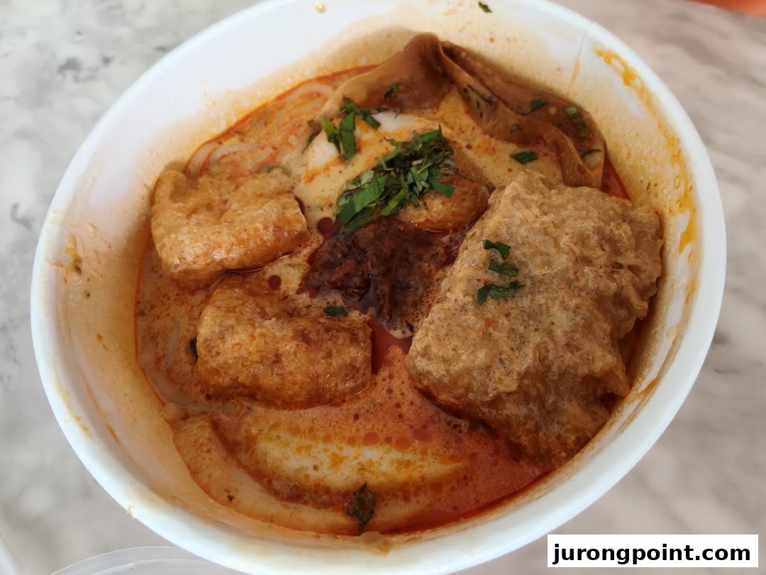 A close-up of a vibrant bowl of curry noodles or laksa with tofu puffs and rich broth.