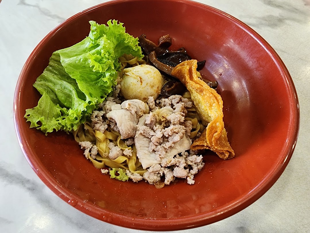 A vibrant red bowl filled with delicious noodles, minced meat, vegetables, and a fried wonton.