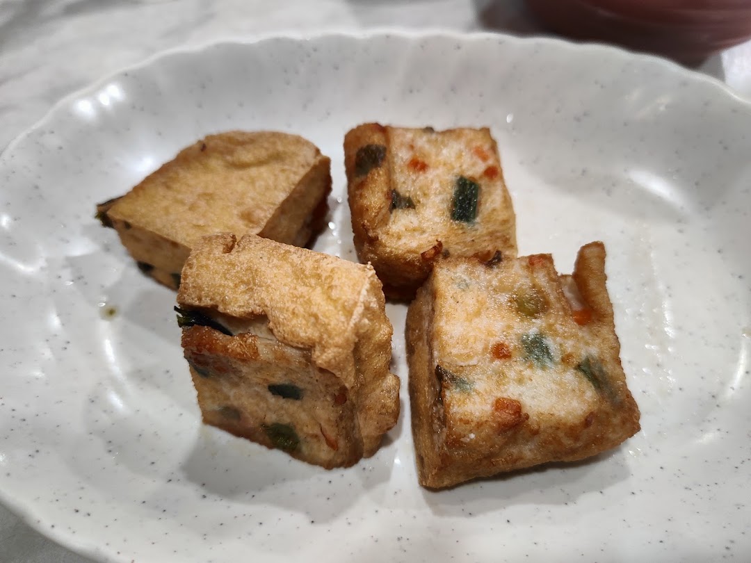 A close-up of four pieces of golden-fried, savory stuffed tofu or fish cakes on a white plate.
