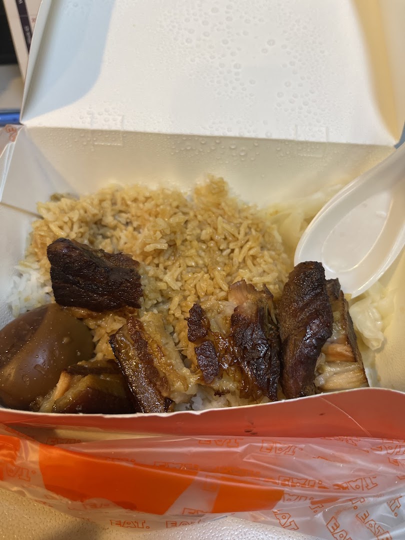 A close-up of a takeaway box filled with braised pork belly, rice, and a braised egg.