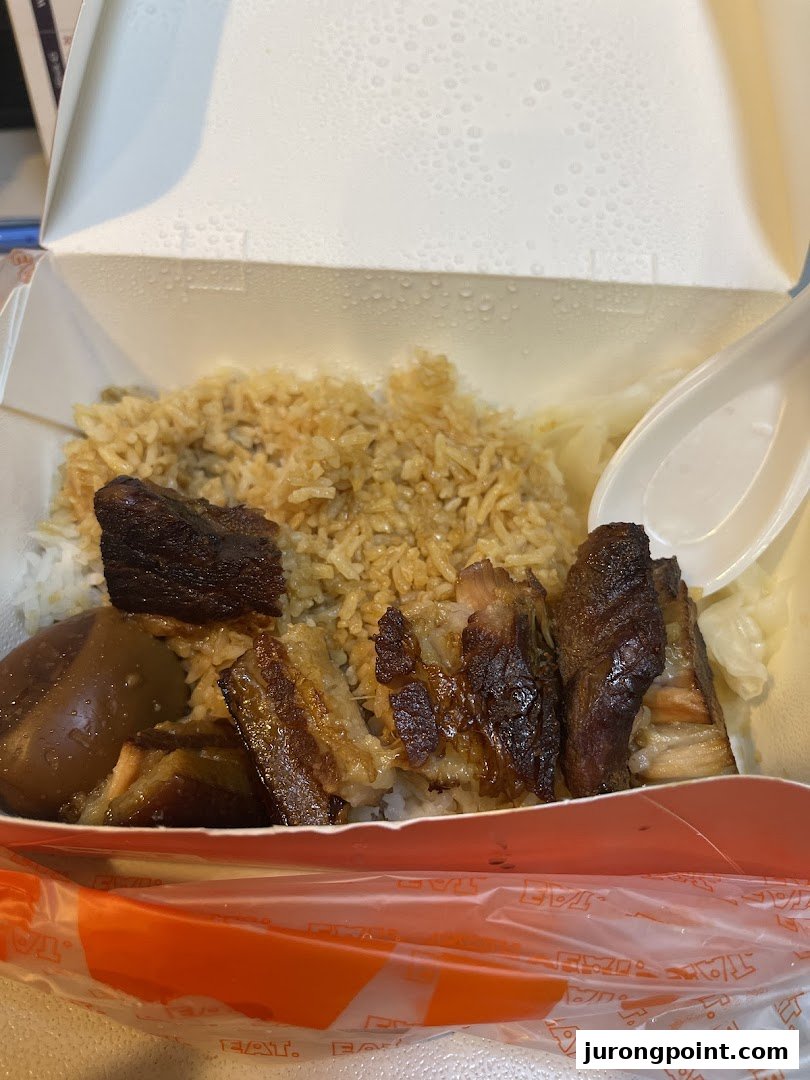A close-up of a takeaway box filled with braised pork belly, rice, and a braised egg.