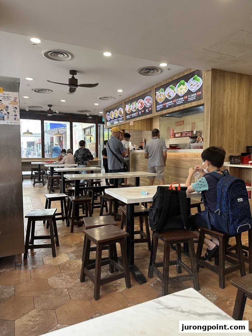 A bustling interior view of EAT, featuring customers, dining tables, and digital menu boards.