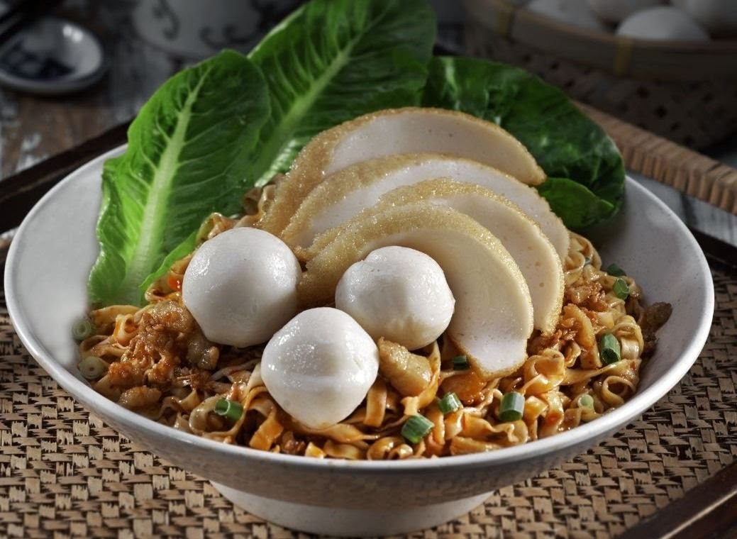 A close-up of a delicious bowl of noodles topped with fish cakes, fish balls, and fresh lettuce.