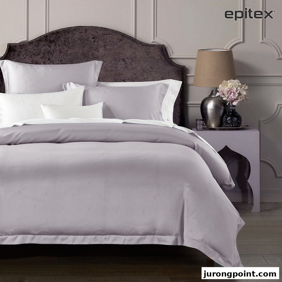 A luxurious bed featuring elegant grey and white bedding with a stylish headboard and bedside decor.