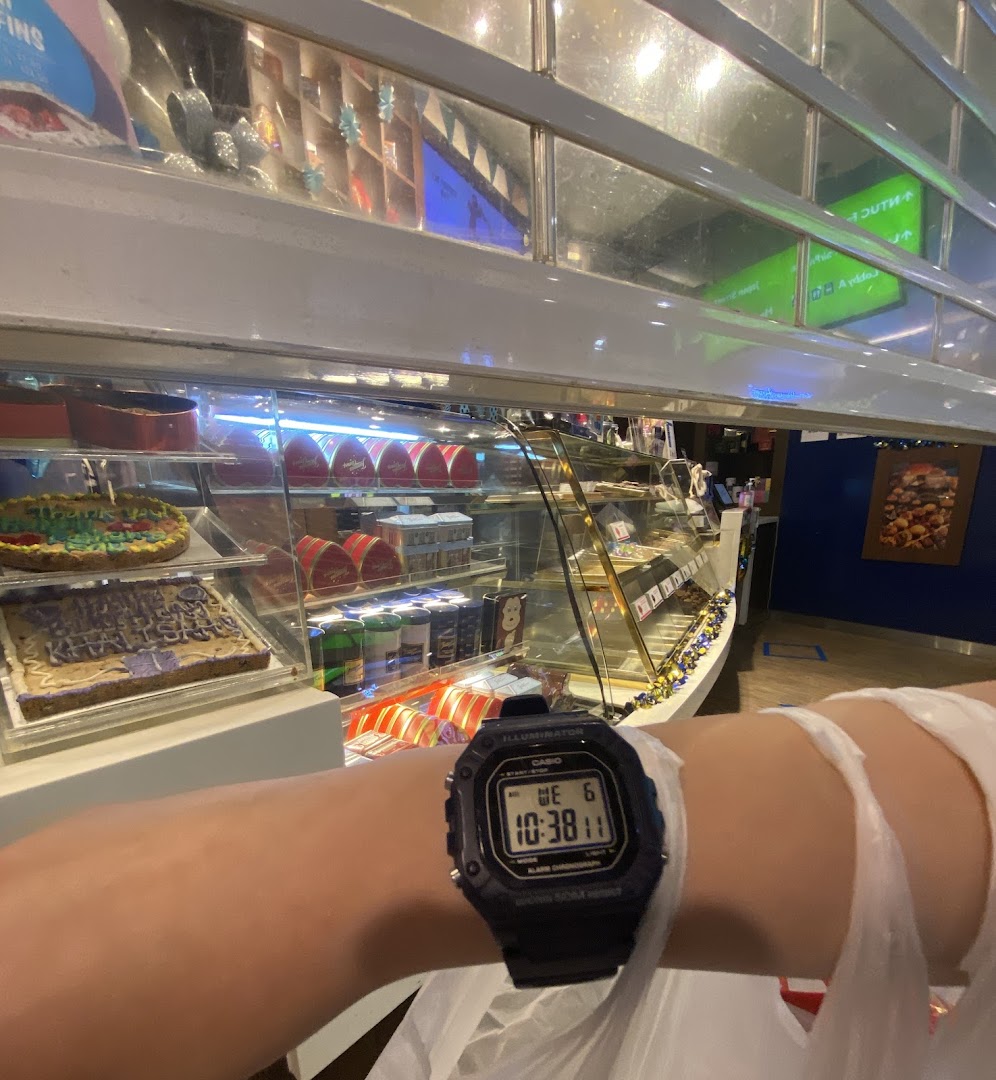 A display case filled with various cookies and baked goods at Famous Amos, with a person's arm and watch in the foreground.
