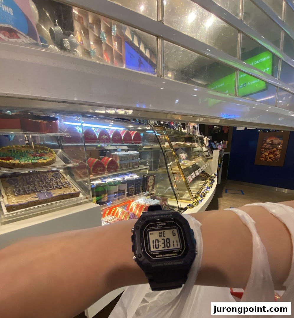 A display case filled with various cookies and baked goods at Famous Amos, with a person's arm and watch in the foreground.
