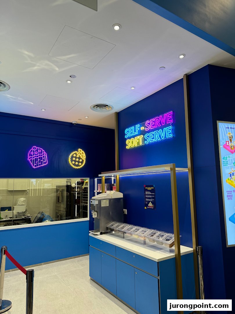 An interior view of Famous Amos featuring a self-serve soft serve station and a visible baking area.