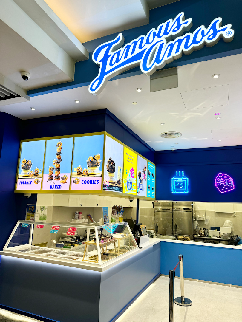 An interior view of a Famous Amos cookie shop featuring its counter, product displays, and vibrant blue branding.