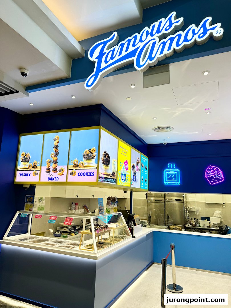 An interior view of a Famous Amos cookie shop featuring its counter, product displays, and vibrant blue branding.