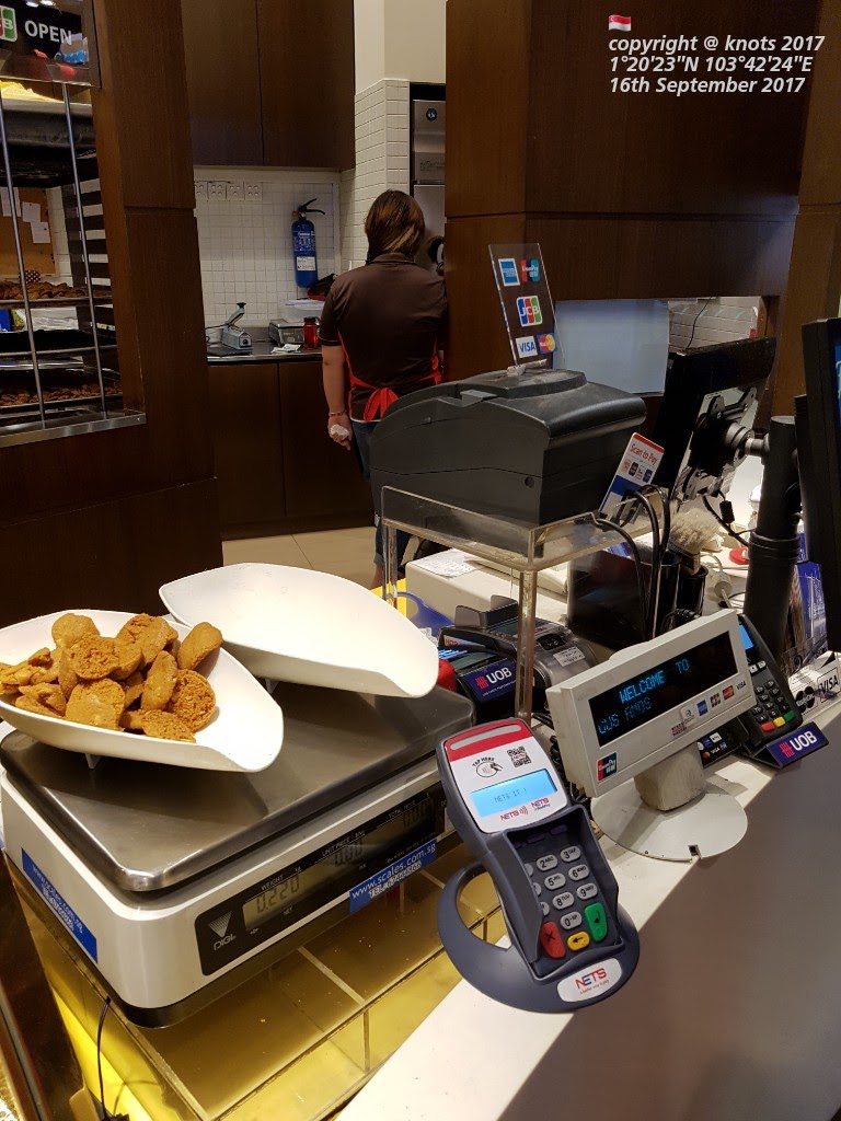 Inside Famous Amos, a counter with cookies on a scale, a payment terminal, and a staff member.