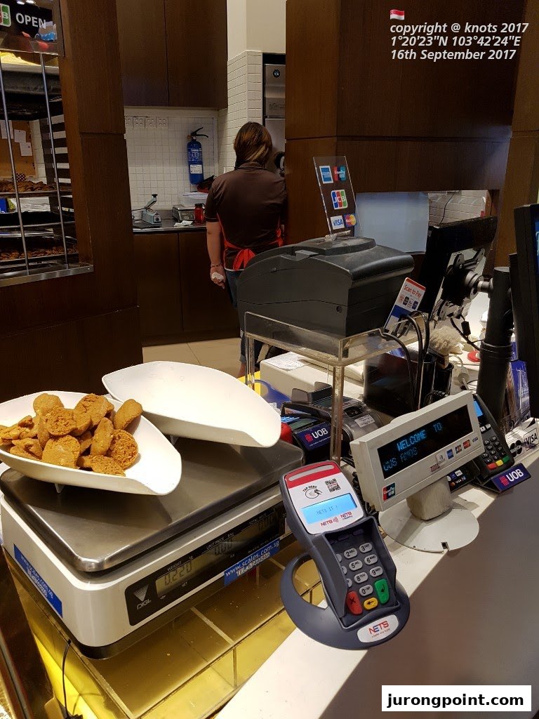 Inside Famous Amos, a counter with cookies on a scale, a payment terminal, and a staff member.