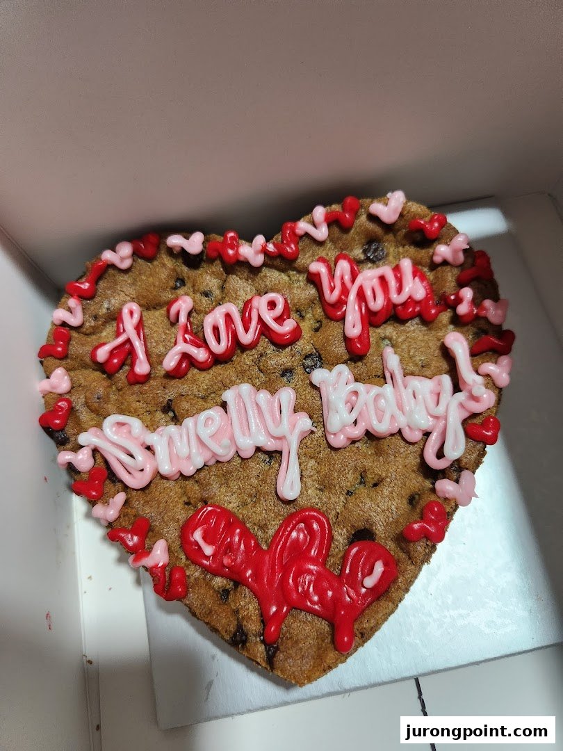 A heart-shaped chocolate chip cookie cake with pink and red icing, saying 'I love you Sweetie Baby!'.