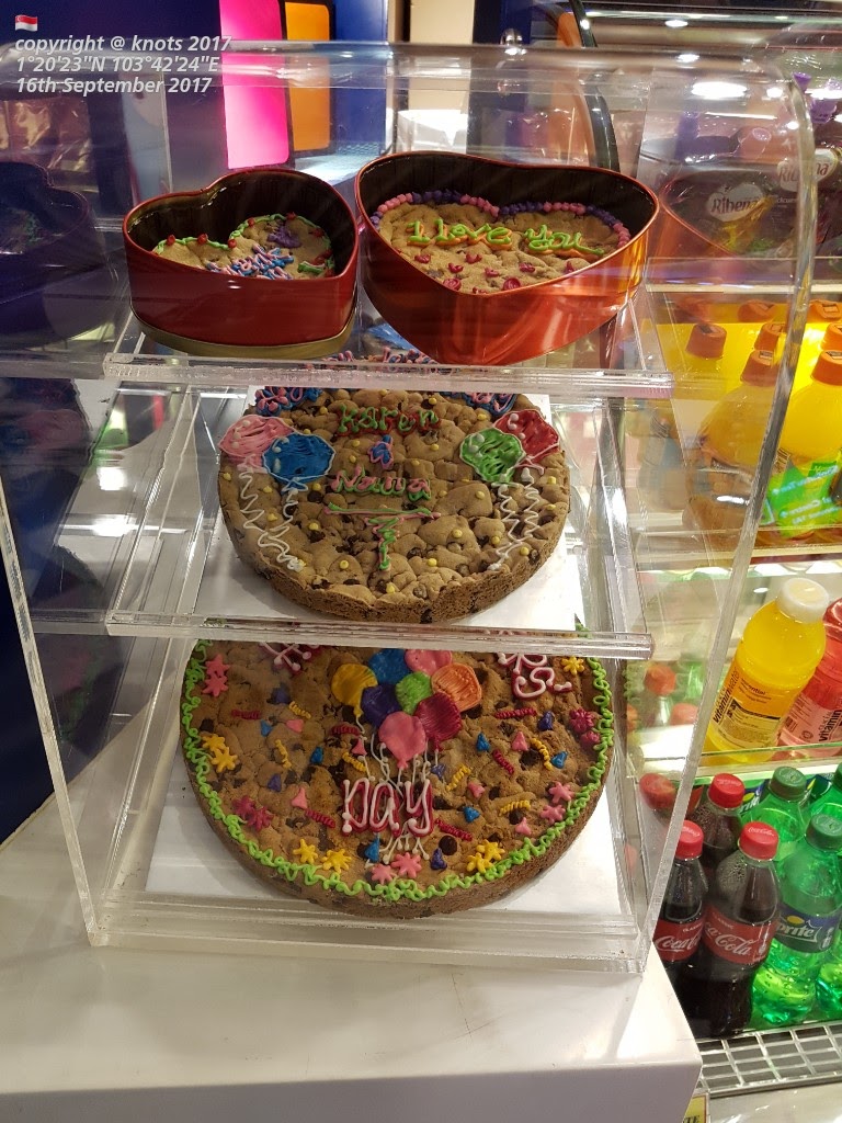 A display case showcasing large, decorated Famous Amos cookie cakes and heart-shaped cookie tins.