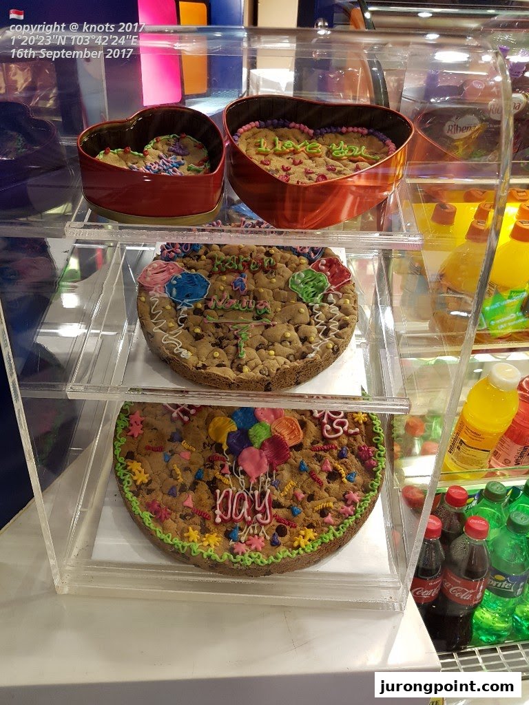 A display case showcasing large, decorated Famous Amos cookie cakes and heart-shaped cookie tins.