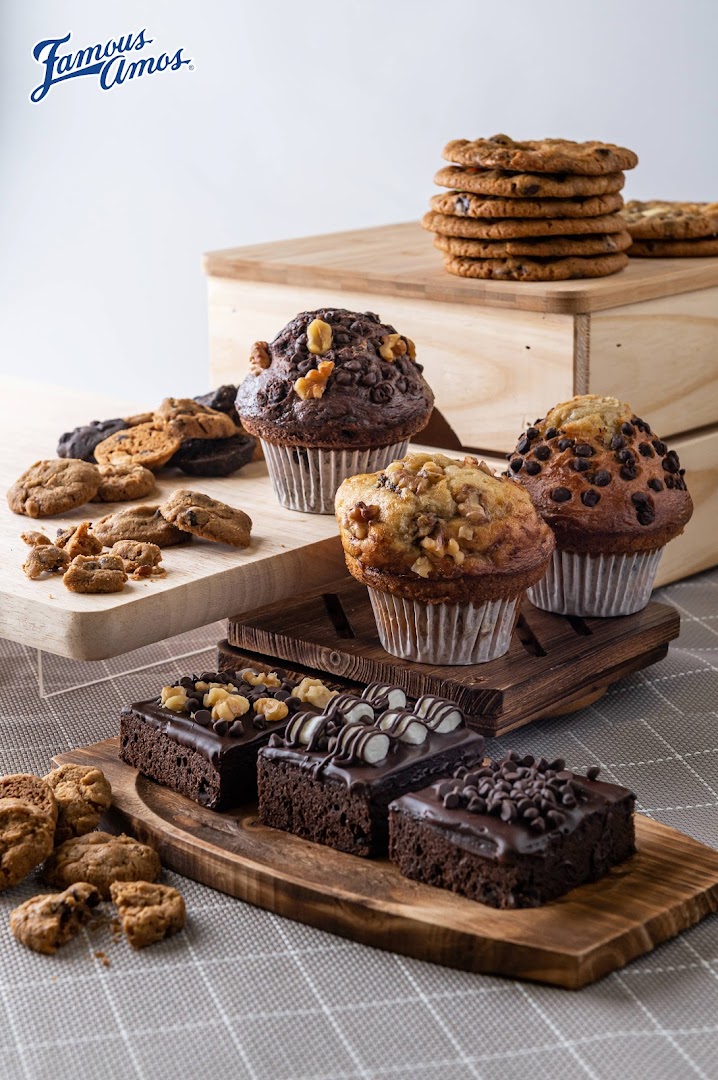 A delicious assortment of Famous Amos cookies, muffins, and brownies displayed on wooden boards.