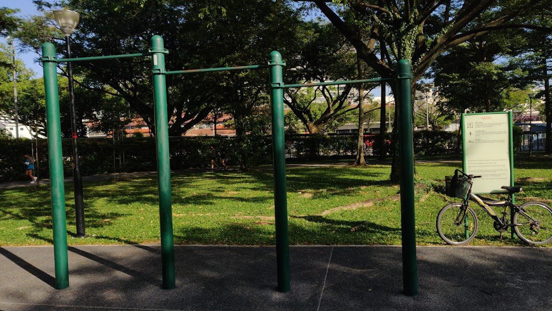 An outdoor park scene featuring green exercise pull-up bars, lush trees, and a bicycle.