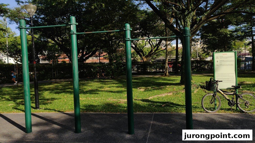 An outdoor park scene featuring green exercise pull-up bars, lush trees, and a bicycle.
