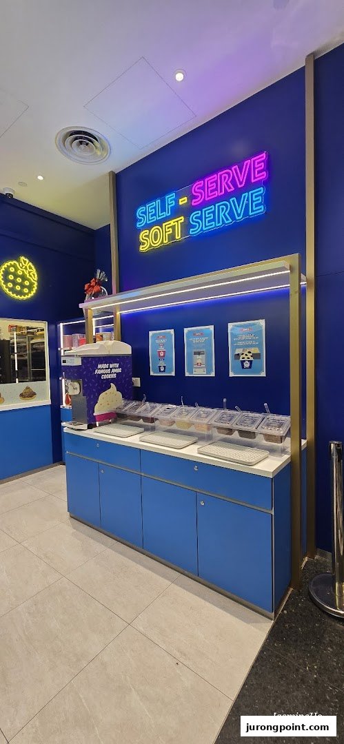 A vibrant Famous Amos shop interior featuring a self-serve soft serve station with various toppings.