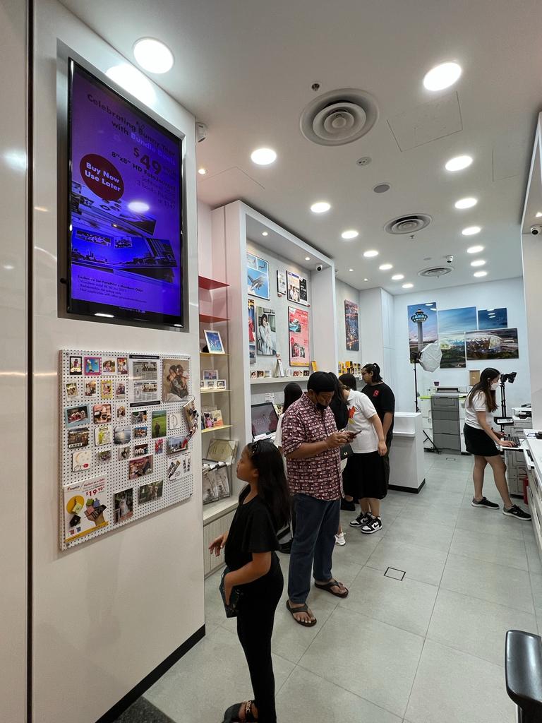 Inside FotoHub, customers browse photo printing services and personalized gifts, with digital displays and product samples.