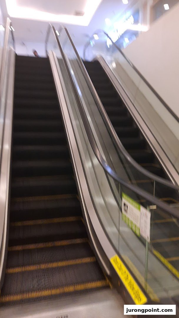 View of escalators in a bright, modern shopping mall interior.