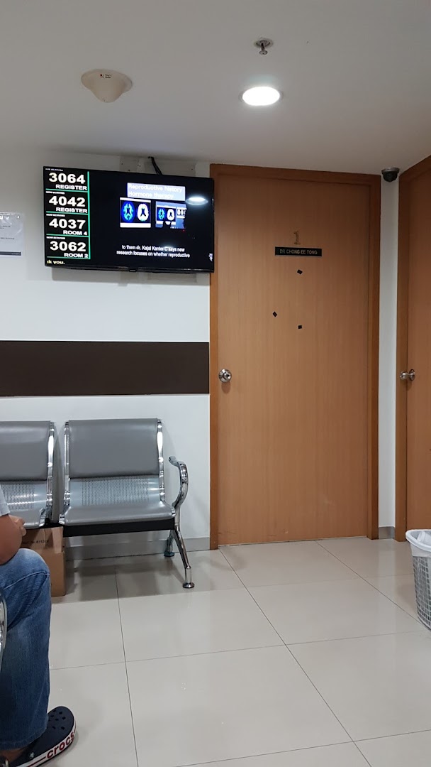 An interior shot of a clinic waiting area with a queue display, TV, and a doctor's office door.