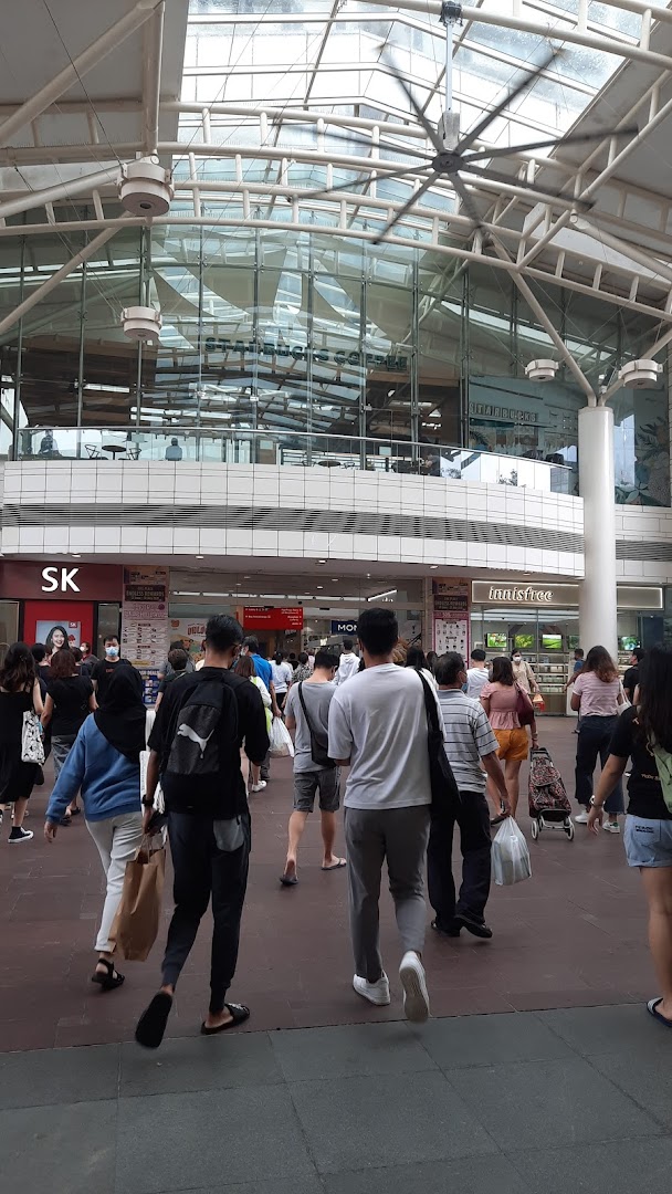 A busy mall walkway with shoppers, leading towards various retail and dining establishments.