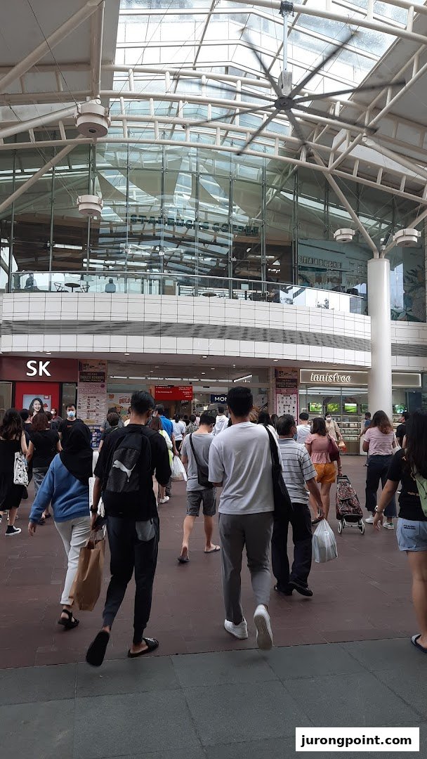 A busy mall walkway with shoppers, leading towards various retail and dining establishments.