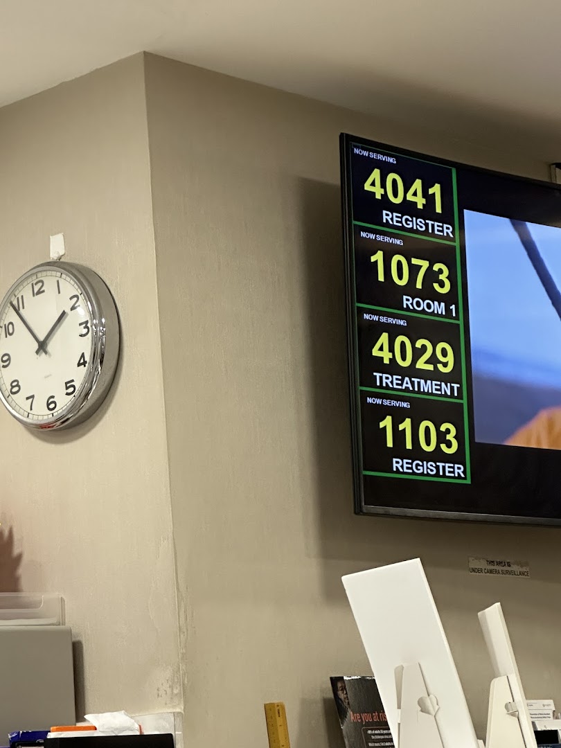 An interior view of Fullerton Health's waiting area, featuring a digital queue display and a wall clock.