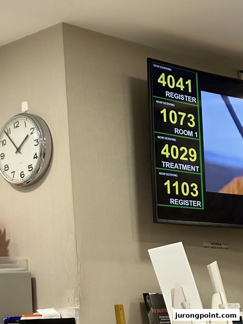 An interior view of Fullerton Health's waiting area, featuring a digital queue display and a wall clock.