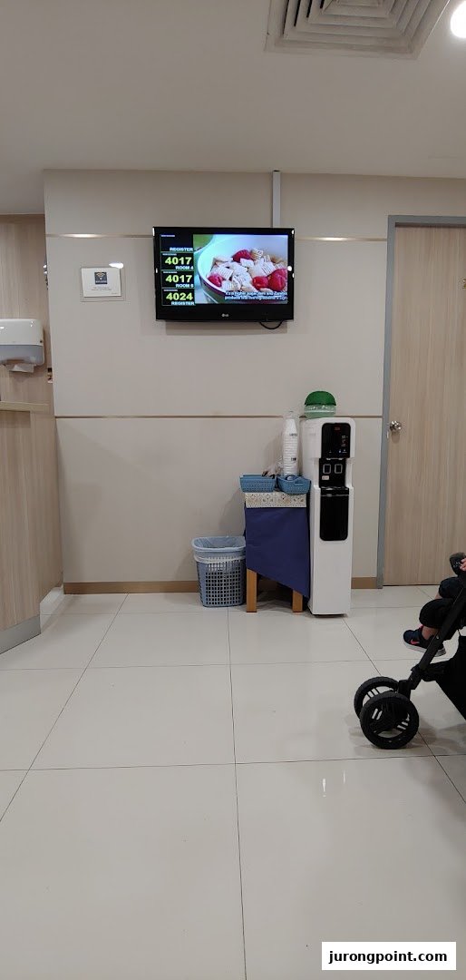 A clean and comfortable waiting area at Fullerton Health, featuring a queue number display and water dispenser.