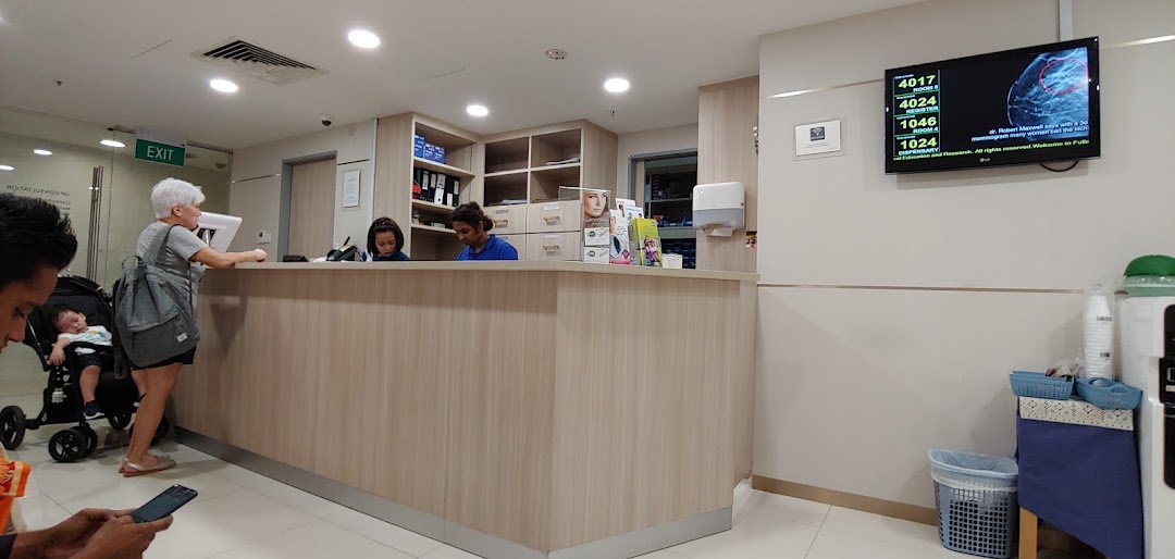 Fullerton Health reception area with staff assisting a patient, featuring a queue number display.