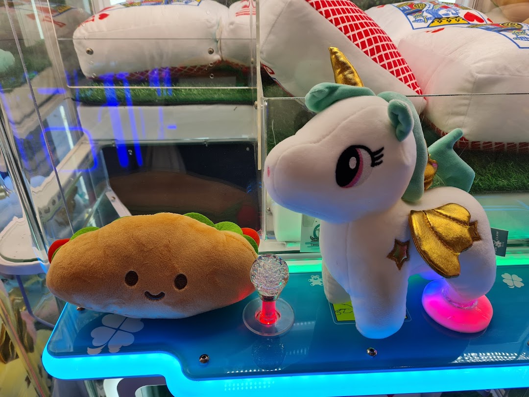Close-up of adorable plush toys, including a taco and a unicorn, inside a brightly lit claw machine.