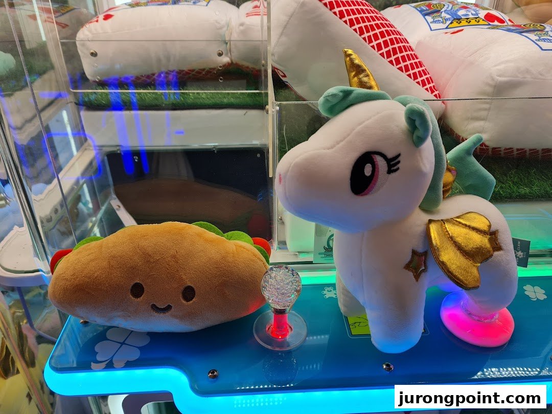 Close-up of adorable plush toys, including a taco and a unicorn, inside a brightly lit claw machine.