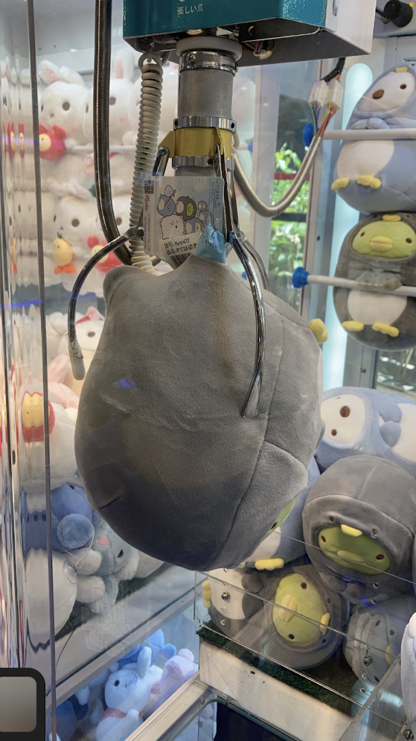 A claw machine's grabber holds a large plush toy, surrounded by other prizes inside the game.